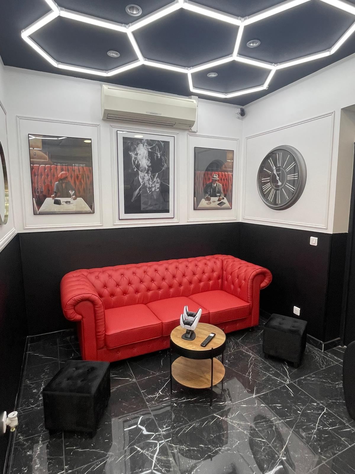 Espace d'attente du barber shop BARBER BON : canapé Chesterfield rouge, tableaux encadrés et plafond lumineux